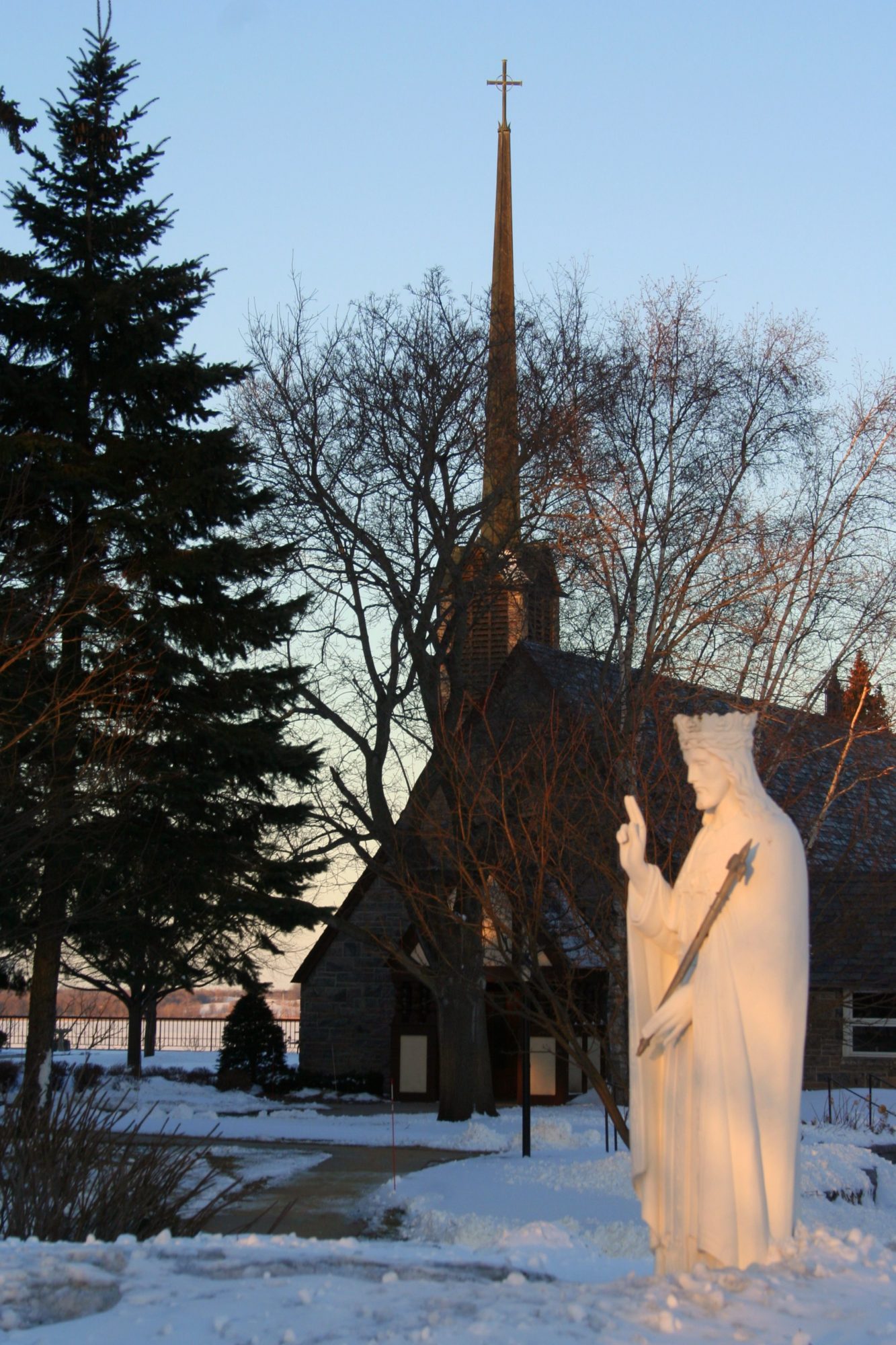 A statue in the snow in front of a church at the lake